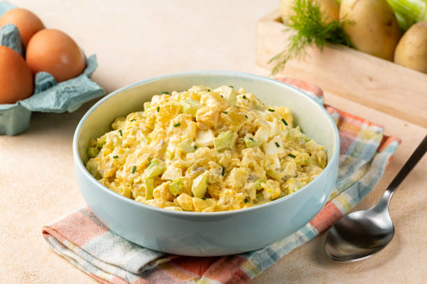Potato salad made from boiled potatoes, boiled eggs, onions, celery, mustard, pickle, mayonnaise and paprika dressing. Ingredients on background.