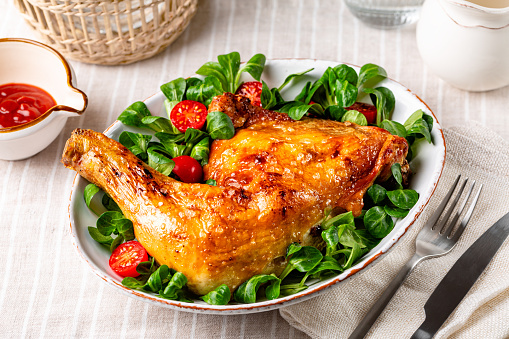 Dinner or lunch, oven roasted chicken leg quarter with fresh valerian or corn salad with cherry tomatoes on white plate.