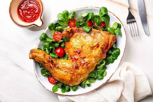 Top view of Dinner or lunch with oven roasted chicken leg quarter and fresh valerian or corn salad with cherry tomatoes on white plate, ketchup.