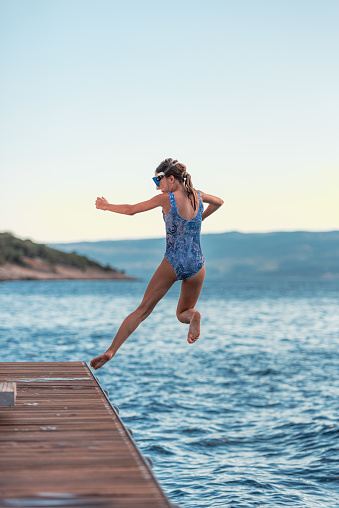 Teenage Girl with Athletic Posture on Summer Vacation on Mediterranean Sea Practice Jumping from the Wooden Pier