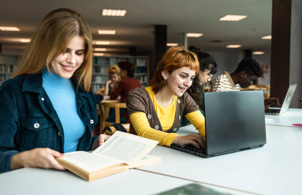 istock Young university students using laptop and reading book in library - School education concept 1969825506