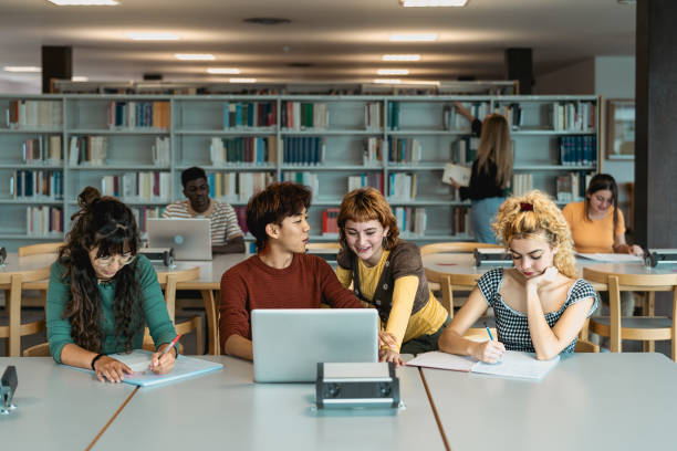 istock Young university students using laptop and studying with books in library - School education concept 1969827660