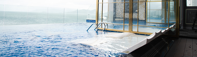 Panorama Infinity pool with white float lounge chairs, handrail, glass wall, ocean and mountain range view at luxury resort hotel in Nha Trang, Vietnam, upscale lifestyle, travel destination. Asia