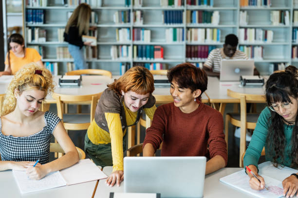 istock Young university students using laptop and studying with books in library - School education concept 1969834732