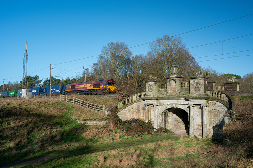 COLWICH, STAFFORDSHIRE, ENGLAND. JANUARY 2024. EWS locomotive train travelling over an ornate railway bridge on the West Coast mainline railway.