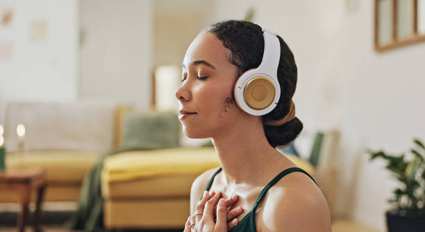 Woman, meditation and yoga in headphones listening to calm music, holistic exercise and peace in living room. Young person with audio podcast, dream of health and relax in spiritual wellness at home stock photo