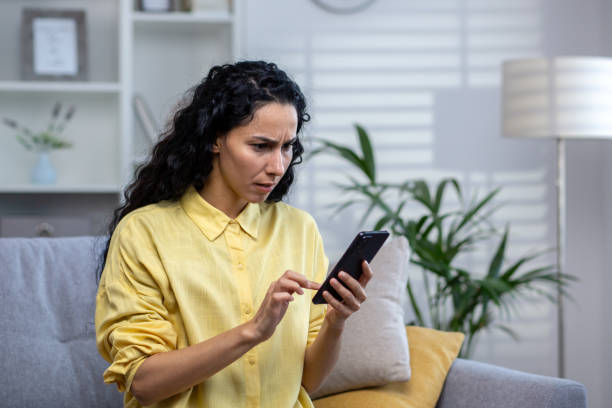 istock Upset and disappointed serious thinking woman alone at home using app on phone close up, hispanic sitting on sofa in living room at home 1969850275