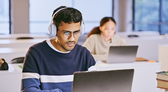 Man, student in headphones and laptop for classroom education, e learning and studying or research in college. People reading and listening on computer for university information or scholarship essay