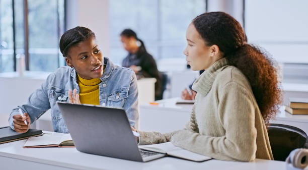 istock College, women and discussion in classroom with laptop for elearning, project or writing study notes. Students, diversity and friends with technology, knowledge or notebook for education and research 1969855093