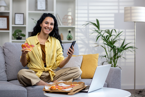 Portrait of happy online food delivery customer shopper woman, Hispanic woman smiling and looking at camera, using app on phone to order pizza delivery.