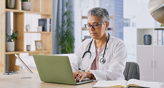 Laptop, doctor and mature woman typing research on healthcare, clinic medicine or medical study. Hospital, computer and surgeon search online for cardiology report, health info or nursing service