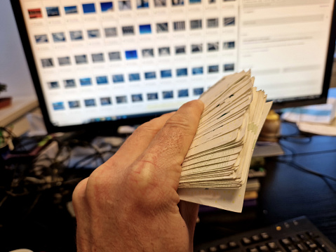 earn money from your computer, become an e-shop owner or a photo contributor. a man holds a large amount of money in his hand in front of a monitor and a keyboard. a roll of banknotes is held by a man, contribution, become, banknote