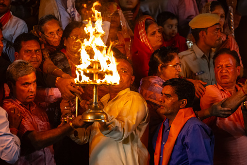 Pushkar, Rajasthan, India - November 2022: Portrait of an hindu male priest performing evening maha aarti (prayer) of holy lake of pushkar called sarovar at pushkar as hindu sanatan rituals.