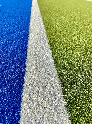 close-up of artificial sports grass. hockey field. green, blue and white grass. rough texture.