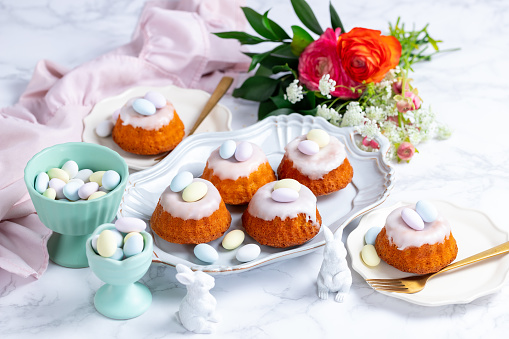 Homemade delicious mini lemon bundt cakes and chocolate eggs on a easter table with fresh spring flowers.