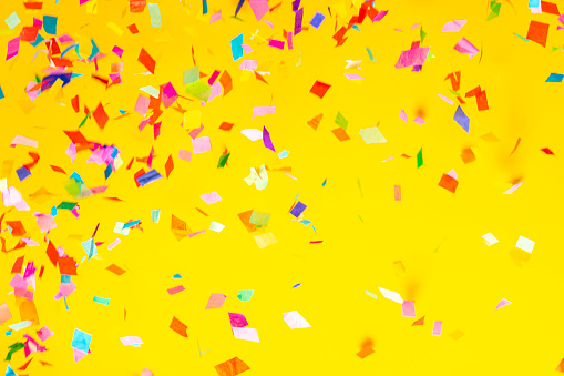 Birthday celebration attributes. Party horns, colorful confetti, candles ice cream cone, cocktail umbrellas & other items on bright yellow background. Close up, top view, copy space, flat lay.