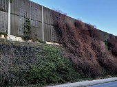on high embankment there is a concrete anti-noise wall with a trellis made of steel mesh. protects residential areas from traffic noise. striped structural surfaces shatter sounds, gabion wall