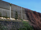 on high embankment there is a concrete anti-noise wall with a trellis made of steel mesh. protects residential areas from traffic noise. striped structural surfaces shatter sounds, gabion wall