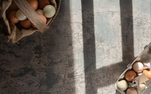 Fresh, heirloom eggs in an antique basket and a paper carton.  Sunlight making shadows from the window onto the counter surface.