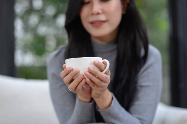 istock Selective focus of relaxed happy young woman's hands holding coffee cup on sofa at home Smiling girl on holiday 1969884840
