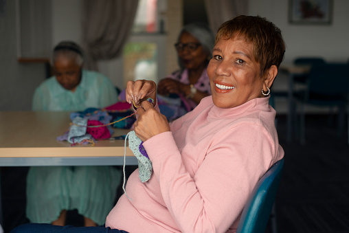 Senior, woman and happy portrait with friends knitting in home with creative community in retirement. Group, craft and African lady smile with crochet, needle or sewing stitch with wool in hands