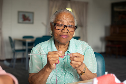 Glasses, knitting and senior woman at her home creating products with wool and needles for hobby. Craft, fun and elderly female person in retirement crocheting items with positive attitude at house.