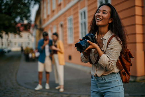 Chinese female tourist gracefully capturing the sights and scenes of the urban landscape with her camera, people in the background