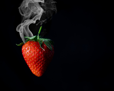 A close-up of a smoking strawberry emitting vaporous fumes from its stem