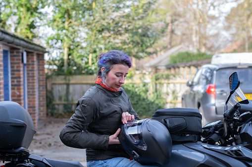 Woman sitting on her motorbike, opening the visor of her helmet, ready to start a trip.
