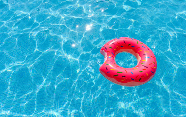 晴れた日のプールの水に浮かぶピンクのインフレータブルサークル。夏休みのコンセプト。ドーナツの形をしたインフレータブルリング。セレクティブフォーカス