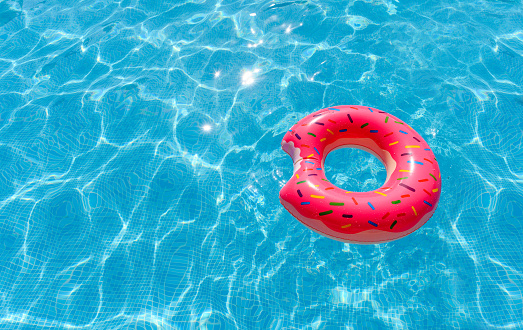 Pink Inflatable circle in the water of the pool on a sunny day. Summer holiday concept. Inflatable ring in the shape of a donut. Selective focus