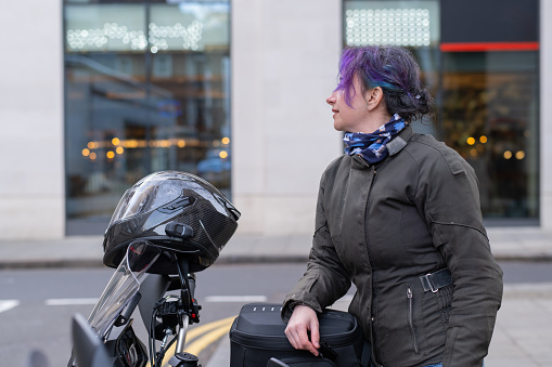 Colored hair woman on her motorbike, standing, looking away, smiling.