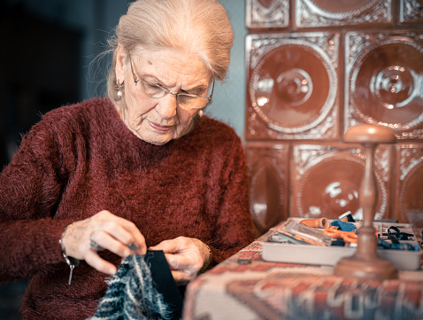 Elderly lady sewing at home. Concentrated with a sewing needle in her hand