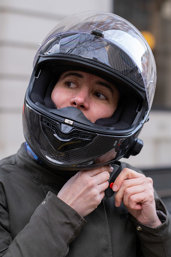 Woman adjusting the strap of her helmet, looking away.