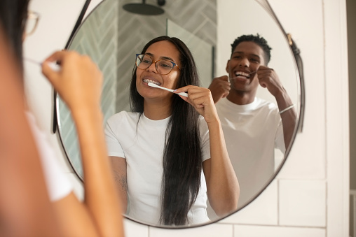 Happy couple, mirror and cleaning teeth for dental hygiene or grooming in bathroom together at home. Face of man and woman with toothbrush and floss for tooth whitening, oral and gum care at house