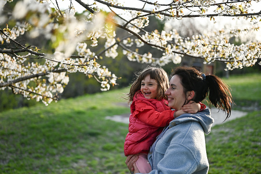 Mother playing with daughter in a spring blossom park.