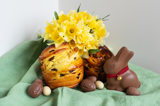 Homemade Easter traditional pastries lie on a green napkin along with daffodil flowers, rabbit, chocolate eggs. Easter baking and decoration