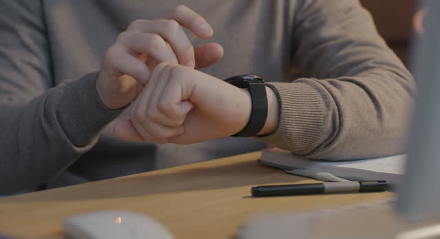 Close-up of male hand using modern touchscreen smart watch at desk in workplace at night