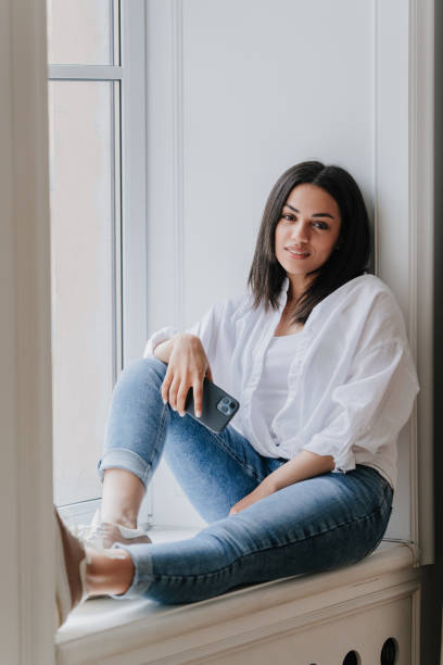 istock Relaxed young woman with smartphone sitting by window 1970024378