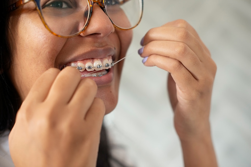 Braces, floss and closeup of woman with dental health, wellness or hygiene morning routine. Smile, dentistry and zoom of young female person cleaning teeth for fresh oral mouth treatment at home.