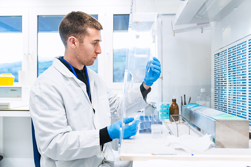 Lab technician carefully inspects the contents of a test tube against the light in a clean, well-equipped hospital laboratory.