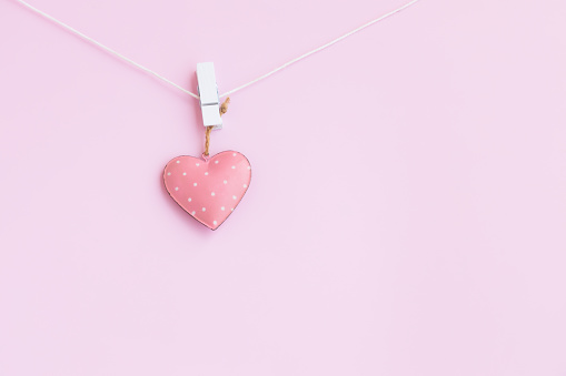 Steel pink heart hanging on a white wooden clothespin and white rope on pink background, Vintage Pink heart shape.