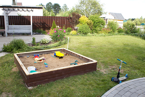 Children's sandbox with different toys and scooter. Playground on green grass. Summer day in the garden lawn.