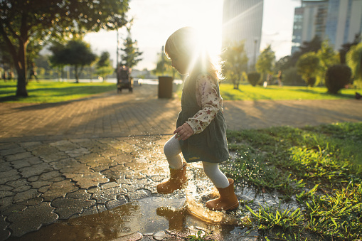 Little girl in rubber boots playing in puddles after rain in springtime or autumn