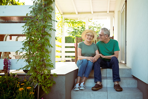 Outdoor portrait of happy senior couple sitting on steps outside house, smiling at camera.