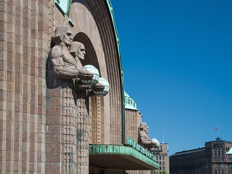 Helsinki Central Railway Station Finland Facade with Art Deco Sculptures - Lyhdynkantajat Sculptures holding copper and glass orbs at the walls of Helsinki Central Station. Monumental Art Deco statues, designed and completed in the year 1914. The Lyhdynkantajat Statues are part of the facade of the Art Nouveau Helsinki Central Station. 100 MPixel Hasselblad X2D Architecture Shot. Helsinki, Finland, Scandinavia, Northern Europe