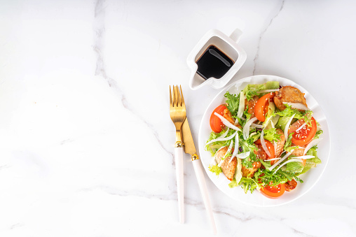 Healthy vegetable green salad with grilled chicken fillet breast, fresh lettuce, tomatoes, onion and balsamic dressing. Spring balanced diet salad on white marble background top view copy space