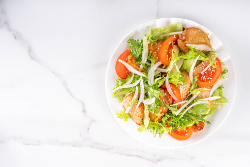 Healthy vegetable green salad with grilled chicken fillet breast, fresh lettuce, tomatoes, onion and balsamic dressing. Spring balanced diet salad on white marble background top view copy space