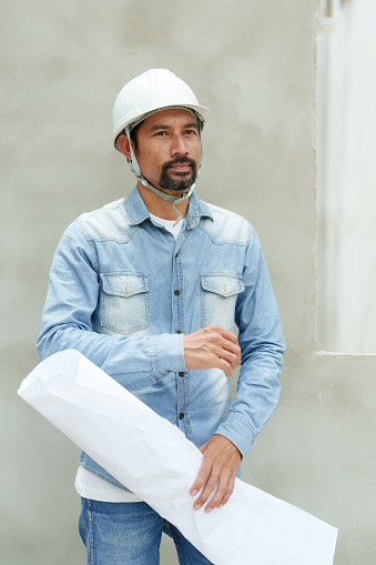 Employees, multiethnic construction workers, engineers wearing safety helmets Stand, change posture and hold the work structure diagram. Look into the camera take photos and supervise construction work.