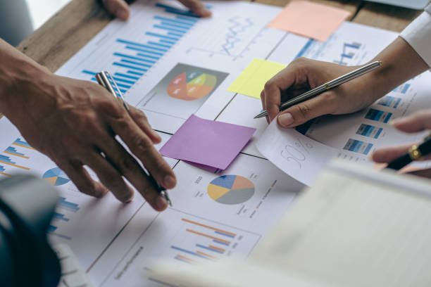 istock Teamwork with business people analyzing cost graphs on a table at a business conference room and office workers working with project planning documents on a conference table, close-up photography 1970247450